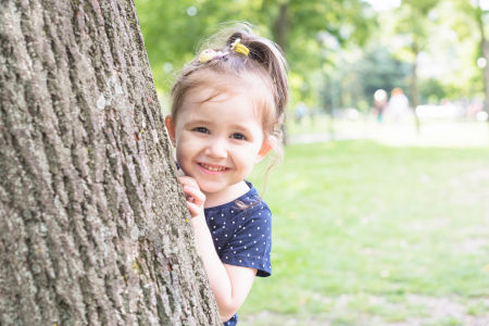 Junges Mädchen versteckt sich hinter einem Baum und lacht